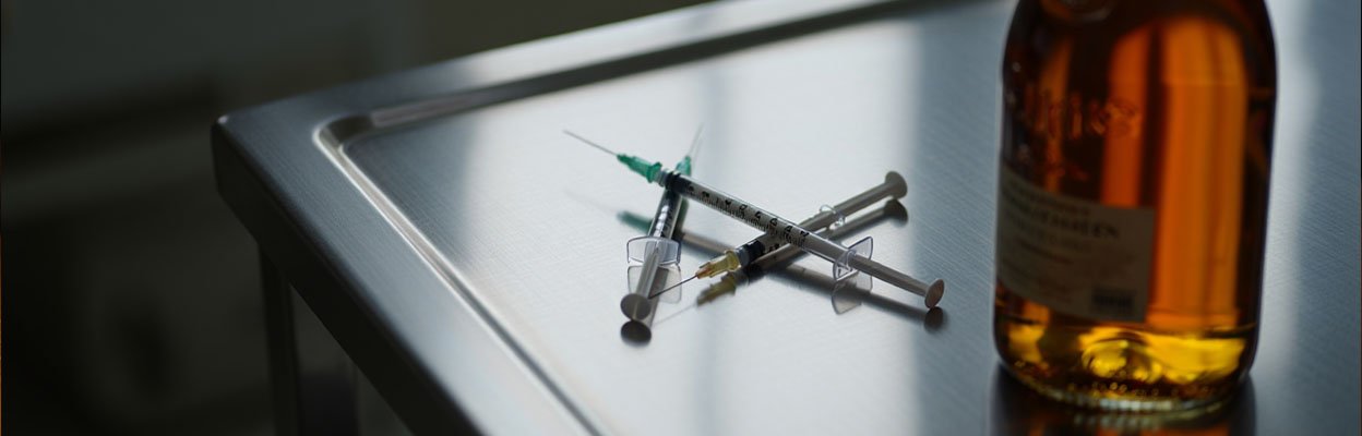 На медицинском столе лежат шприцы и стоит бутылка коньяка